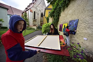 Brigádníci v červených tričkách instalují obrazy ve Františkánské zahradě