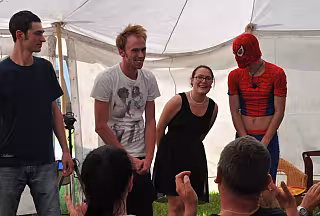 Dospělí a osoba v kostýmu Spider-Mana baví děti pod stanem na venkovní oslavě