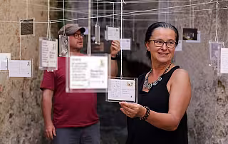 Žena a muž drží papíry v místnosti s visícími šňůrami a zavěšenými dokumenty.