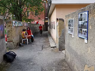 Vnitřní dvůr s budovou, kde sedí dělník v oranžové vesty, kolem jsou krabice a vozík.