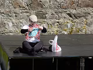 Dítě v barevném tričku sedí na černé lavici před kamennou stěnou a drží míč.