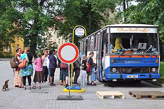 Lidé stojí ve frontě u modrého autobusu přeměněného na pojízdný obchod na městském chodníku