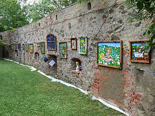 Kamenná zeď pokrytá barevnými obrázky a kresbami, zelený trávník vpředu, zeleň v pozadí.