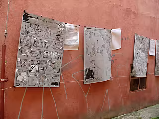 Čtyři zvetšené plány nebo mapy připevněné na terrakótové zdi.