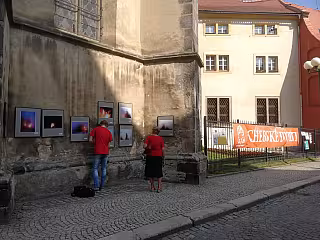 Dvě osoby sledují venkovní výstavu fotografií na zdi budovy ve městě.