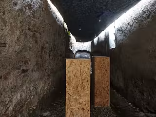 Tmavý kamenný tunel se dvěma dřevěnými deskami opřenými o zeď.
