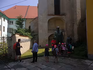 Skupina lidí s dětmi před bronzovou sochou u historické budovy