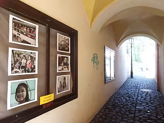 Fotografie lidí na zdi chodby s klenutým průchodem a dlažebními kostkami.