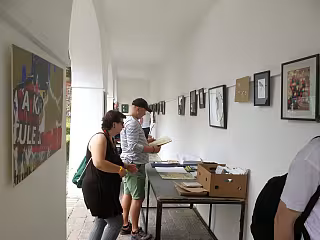 Lidé prohlížejí výstavu fotografií v osvětlené chodbě s obrazy na stěnách.