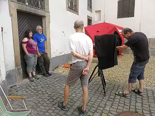 Dva muži fotografují pár před budovou pomocí velkého červeného stanu na světlo.