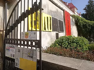 Budova s červenými dveřmi, žlutými okny a kovovým plotem před ní.