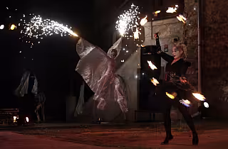 Ohňová show v noci, performer s hořícími tyčemi a létající ohnivé jiskry.