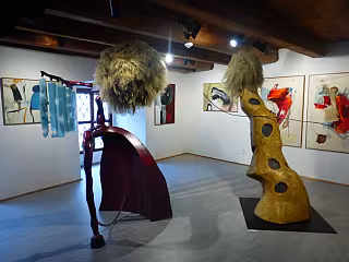 Výstavní sál s abstraktními sochami a malbami na bílých stěnách galerie.