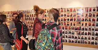 Skupina mladých lidí si prohlíží stěnu pokrytou desítkami barevných fotografií v galerii