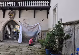 Nádvoří historické budovy s arkádovým balkonem, sušícím se prádlem na šňůře a zeleným keřem